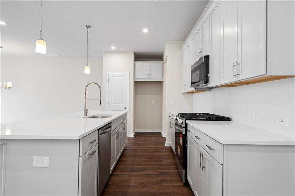 Modern kitchen with white shaker cabinets, large quartz island sink, stainless appliances, hardwood floors in The Cary B, Kennesaw, GA