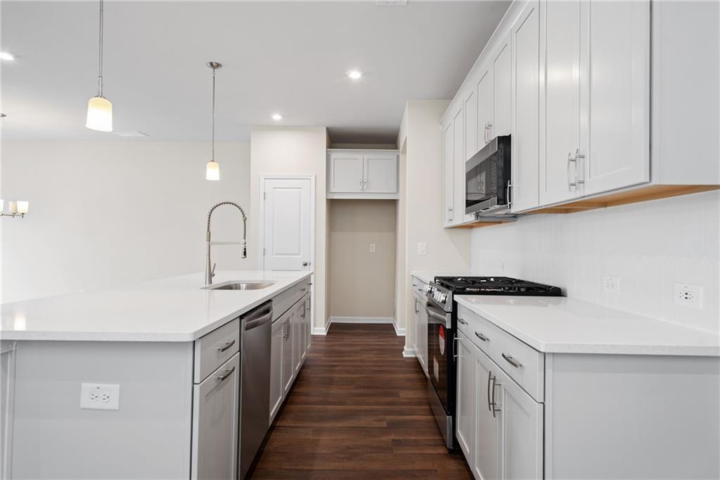 Modern kitchen with white cabinets, quartz island sink, stainless appliances, hardwood floors in Davidson Homes The Cary B, Kennesaw, GA