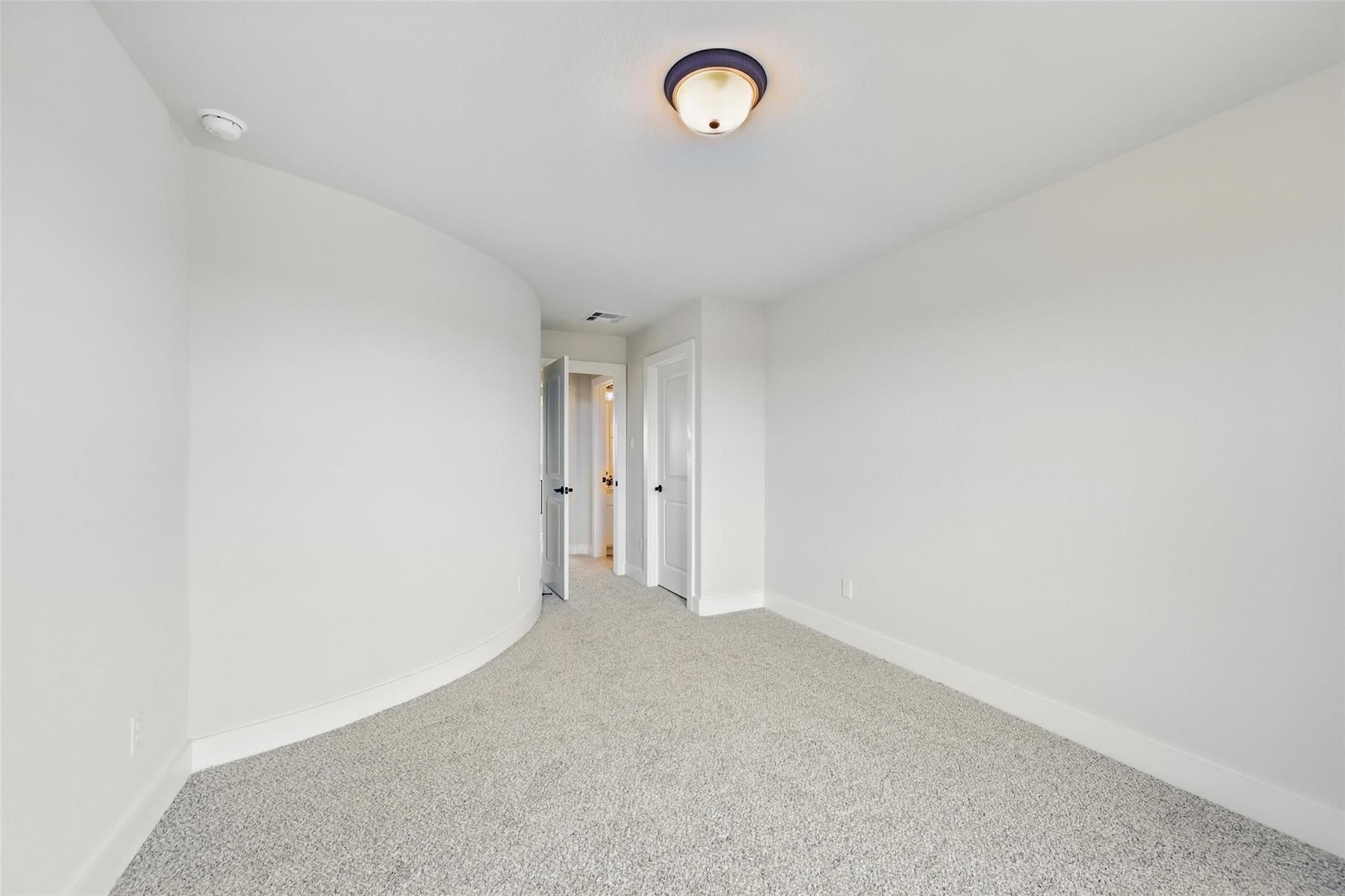 Empty bedroom featuring curved white walls, gray carpet flooring, and double doors in Davidson Homes The Victoria C, Lago Mar, Texas City