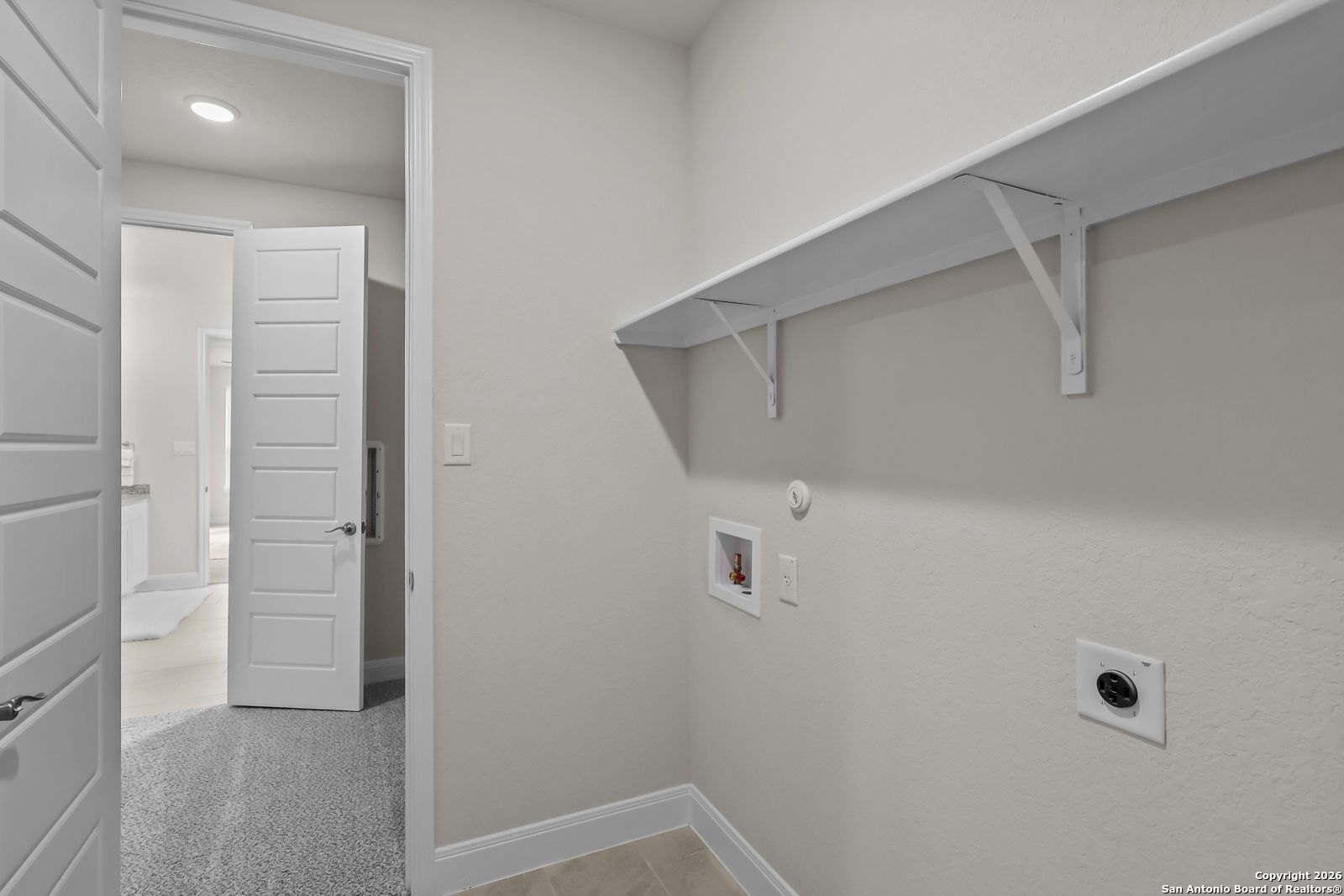 Spacious laundry room with built-in white shelves and washer-dryer hookups in The Lanier H by Davidson Homes, Ladera, San Antonio