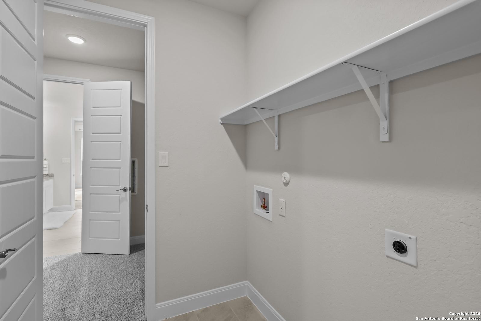 Spacious laundry room with built-in white shelves and washer-dryer hookups in The Lanier H by Davidson Homes, Ladera, San Antonio