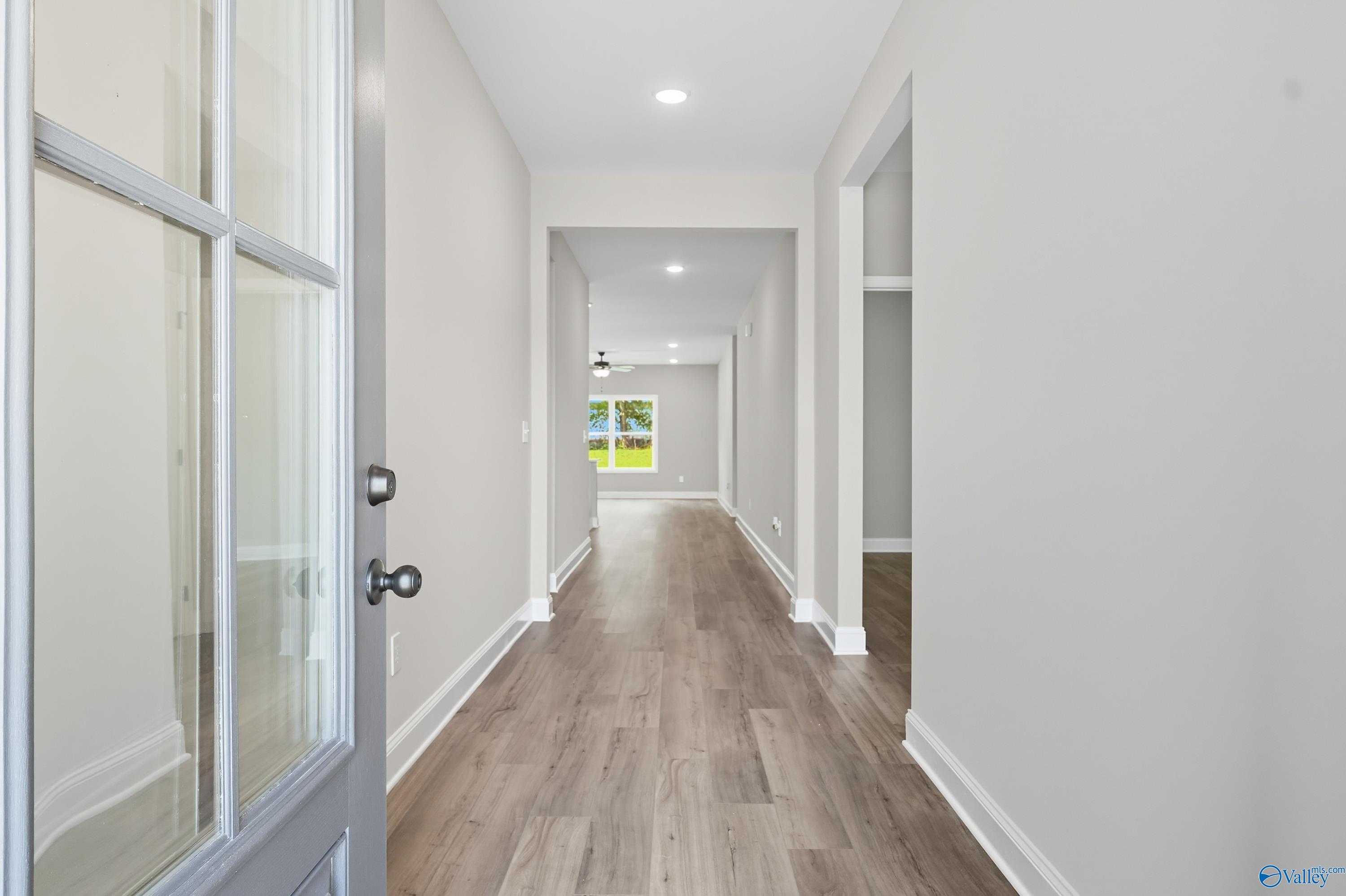 Spacious entry hallway with hardwood floors, neutral walls, and backyard view through window in The Daphne 4-bedroom home, Meridianville, Alabama