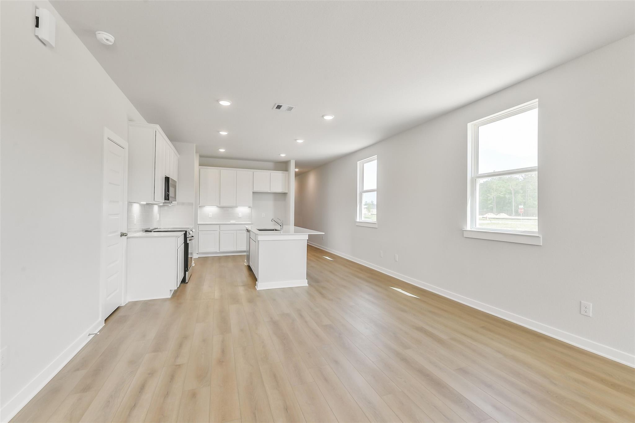 Modern white kitchen island with stainless appliances and recessed lighting in open living space, The Frio G by Davidson Homes, Conroe TX