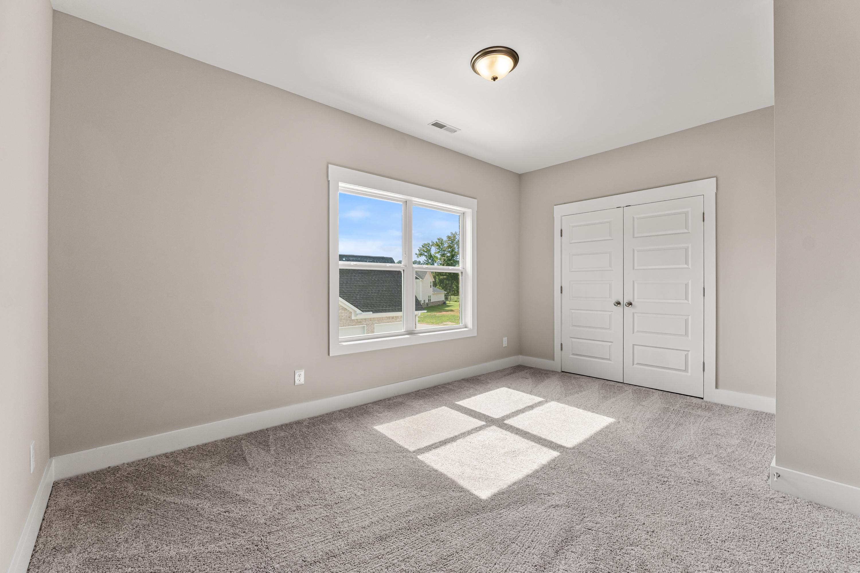 Spacious secondary bedroom in The Oxford C featuring beige walls, large window with natural light, carpeted floor, and double closet doors
