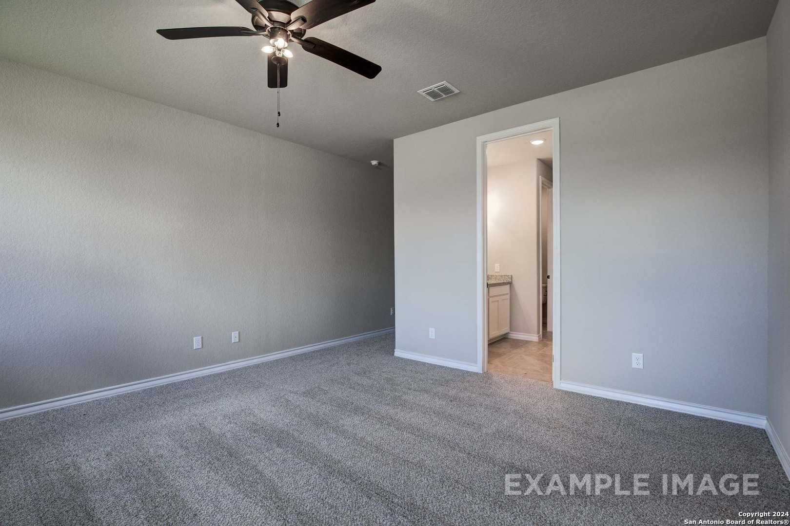 Spacious empty master bedroom with ceiling fan, gray carpet, and open en-suite bathroom in Davidson Homes The Rockford G, Ladera, San Antonio