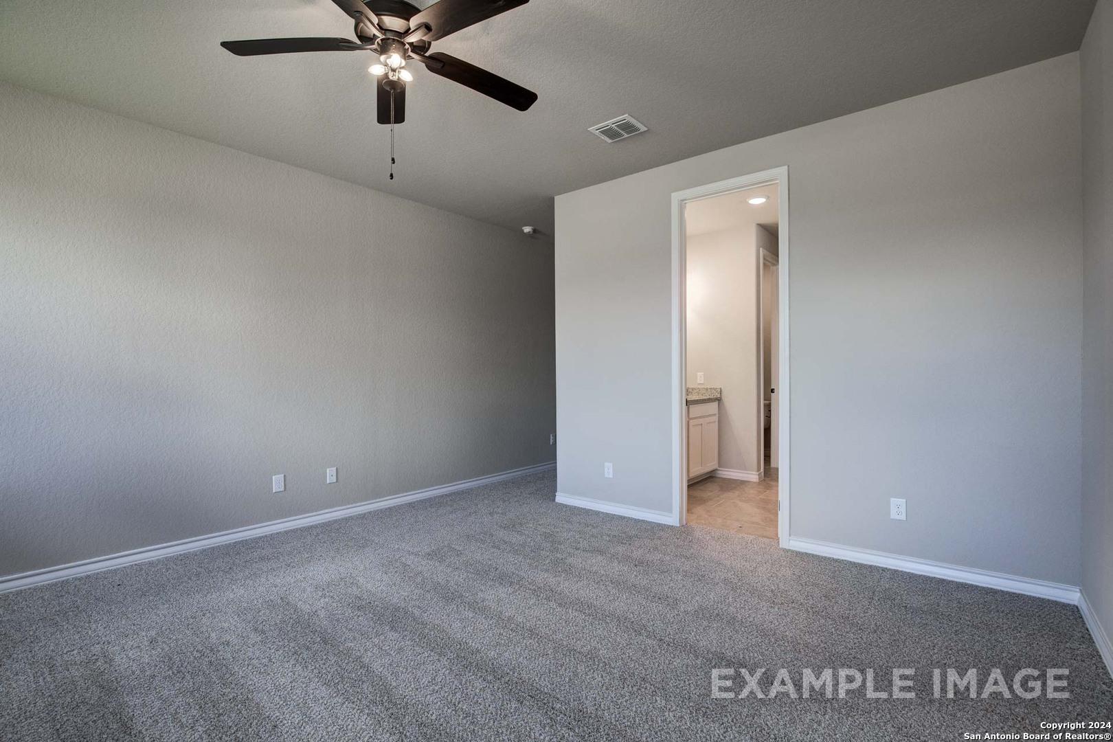 Spacious empty master bedroom with ceiling fan, gray carpet, and open en-suite bathroom in Davidson Homes The Rockford G, Ladera, San Antonio