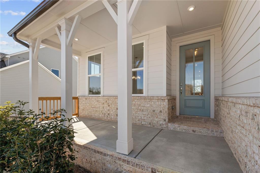 Inviting covered front porch with white columns, glass entry door, and brick base on Davidson Homes Willow B in Wehunt Meadows, Hoschton, Georgia
