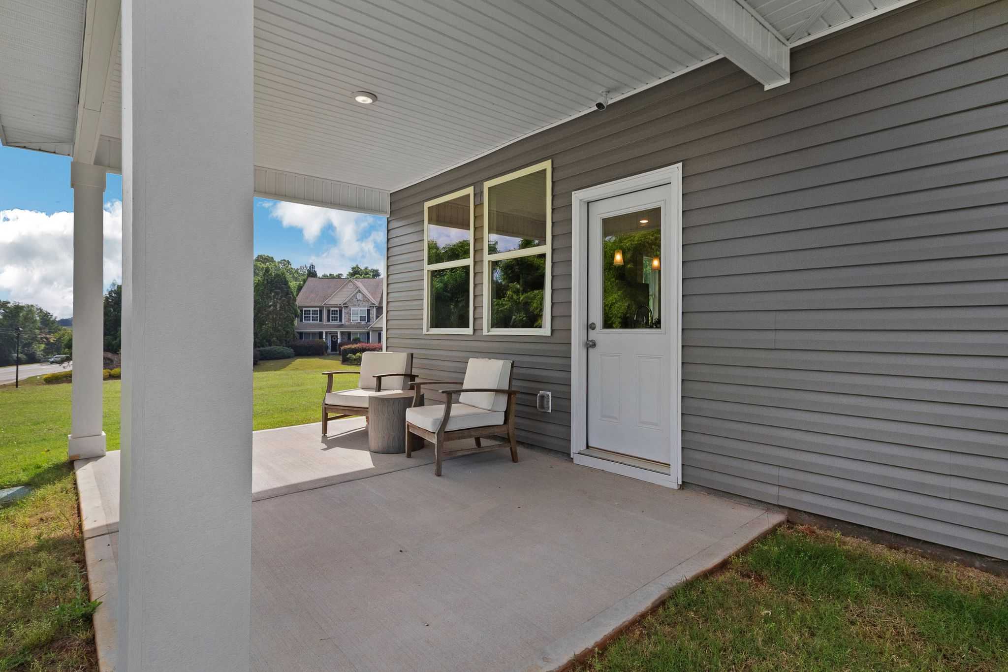 Covered porch with wicker chairs and table at Ivy Glen in Perry GA, gray siding home exterior and green lawn