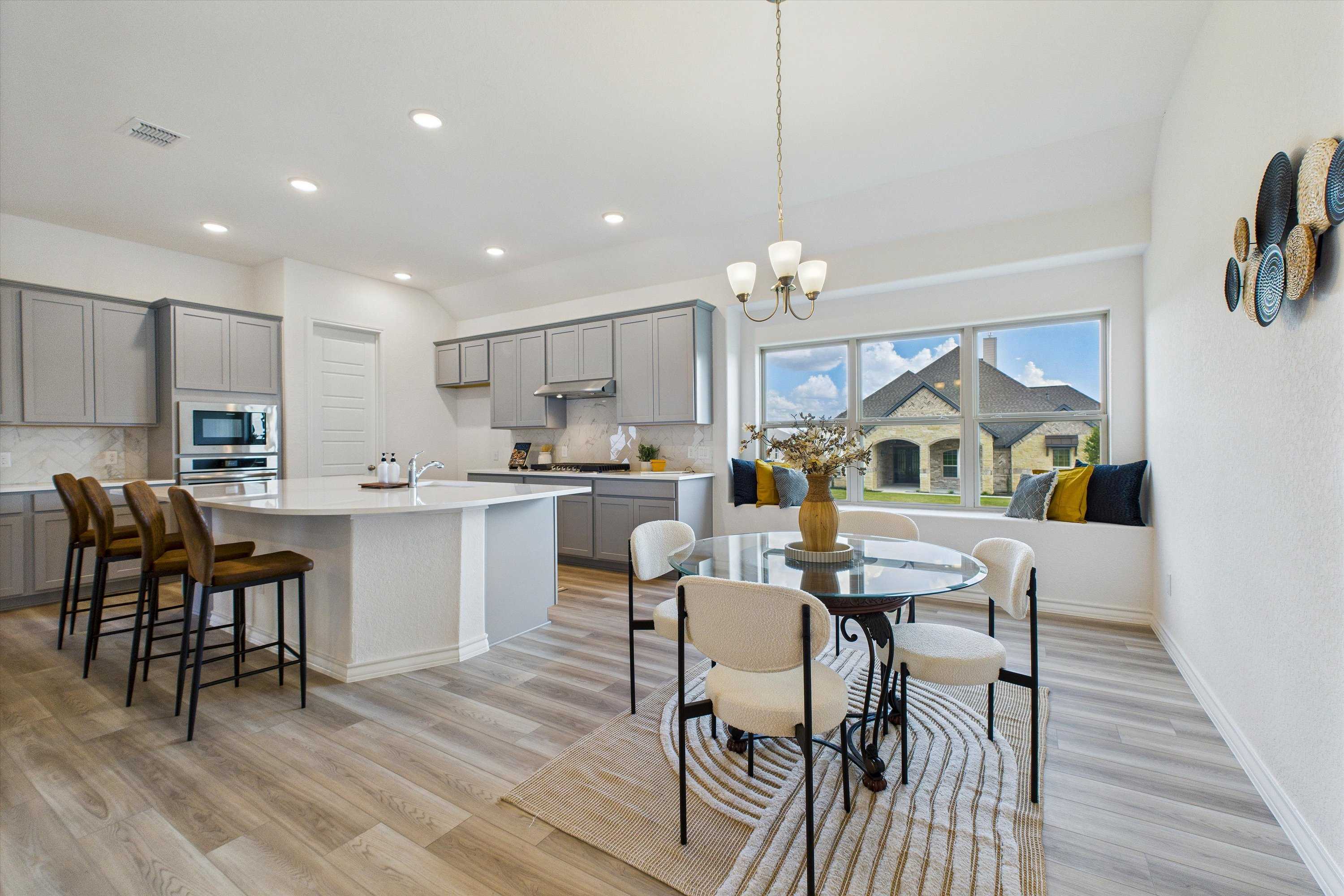 Modern open-concept kitchen with gray cabinets, white island, and dining table by large windows in The Summerlin C, Castroville, Texas