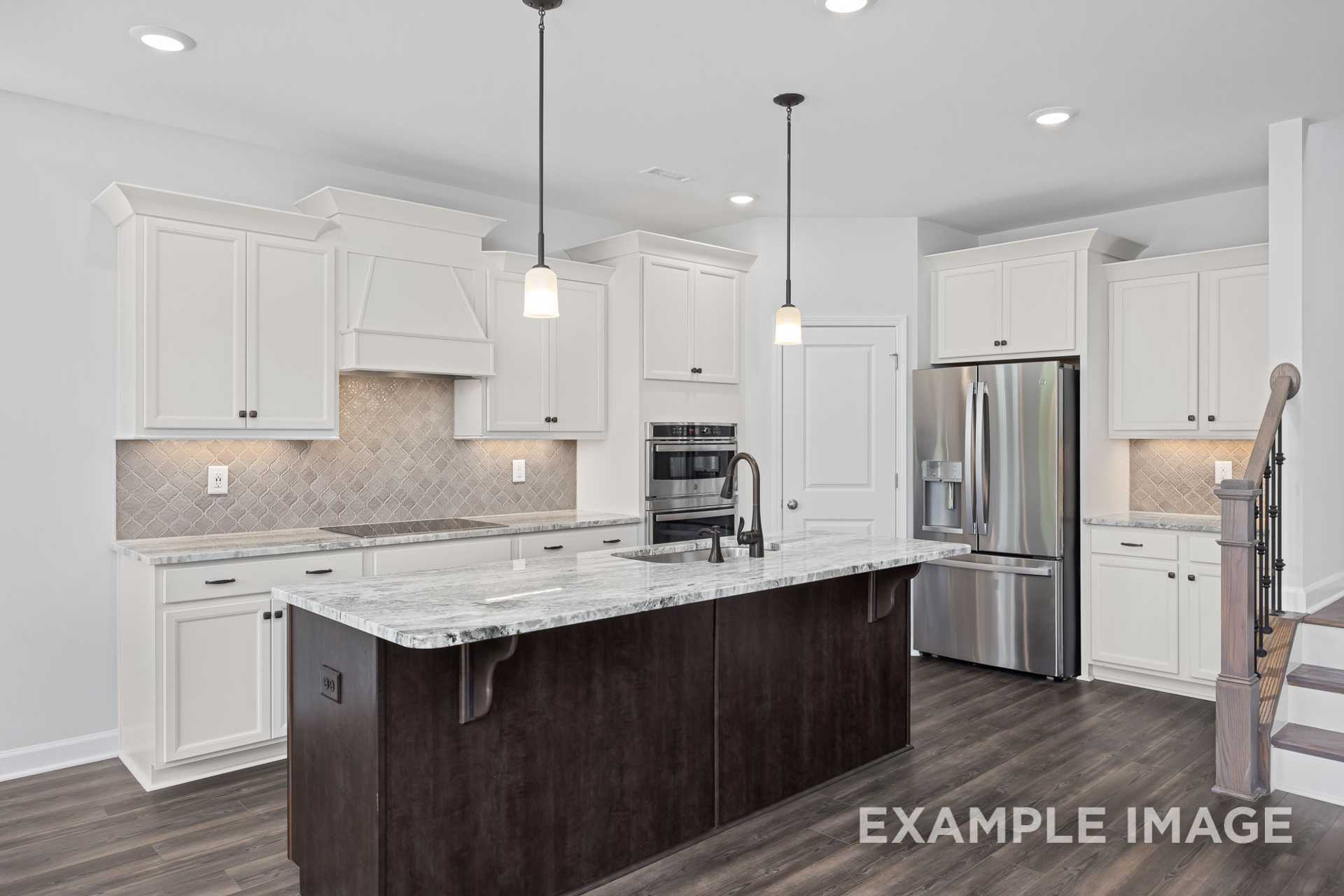 Modern kitchen in The Grace C showcasing white shaker cabinets, large center island, stainless steel appliances, subway tile backsplash