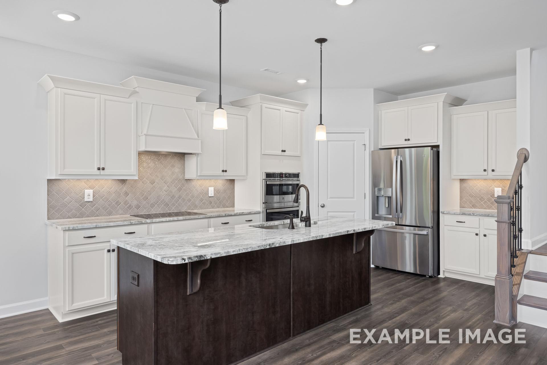 Modern kitchen in The Grace C showcasing white shaker cabinets, large center island, stainless steel appliances, subway tile backsplash