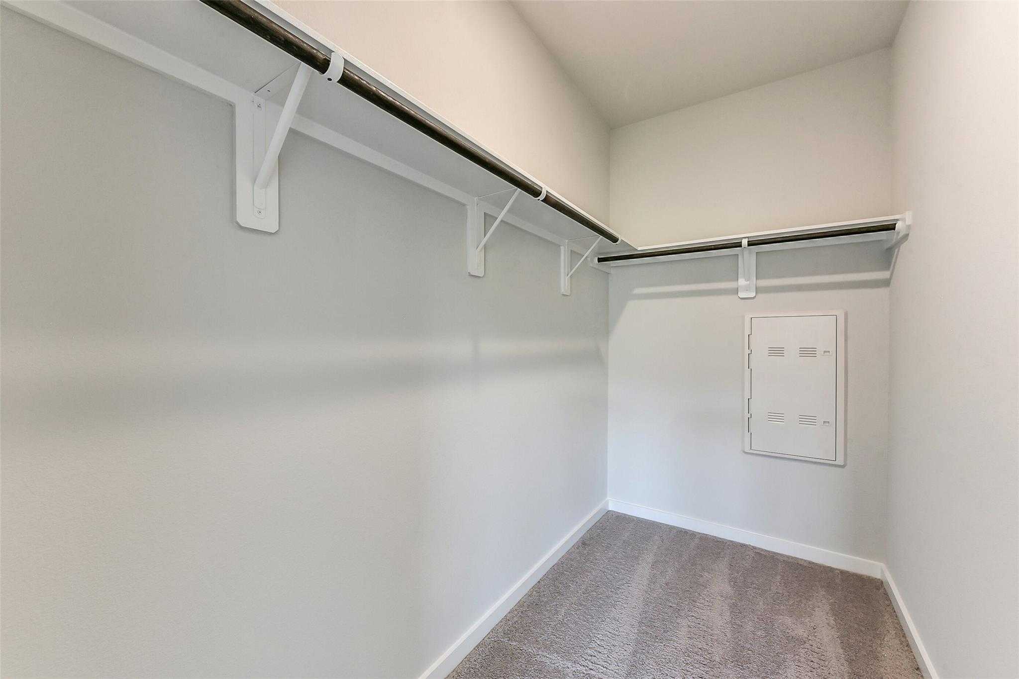 Spacious walk-in closet with double hanging rods, shelves, neutral walls, and carpet in Davidson Homes The Frio F, Dayton, Texas