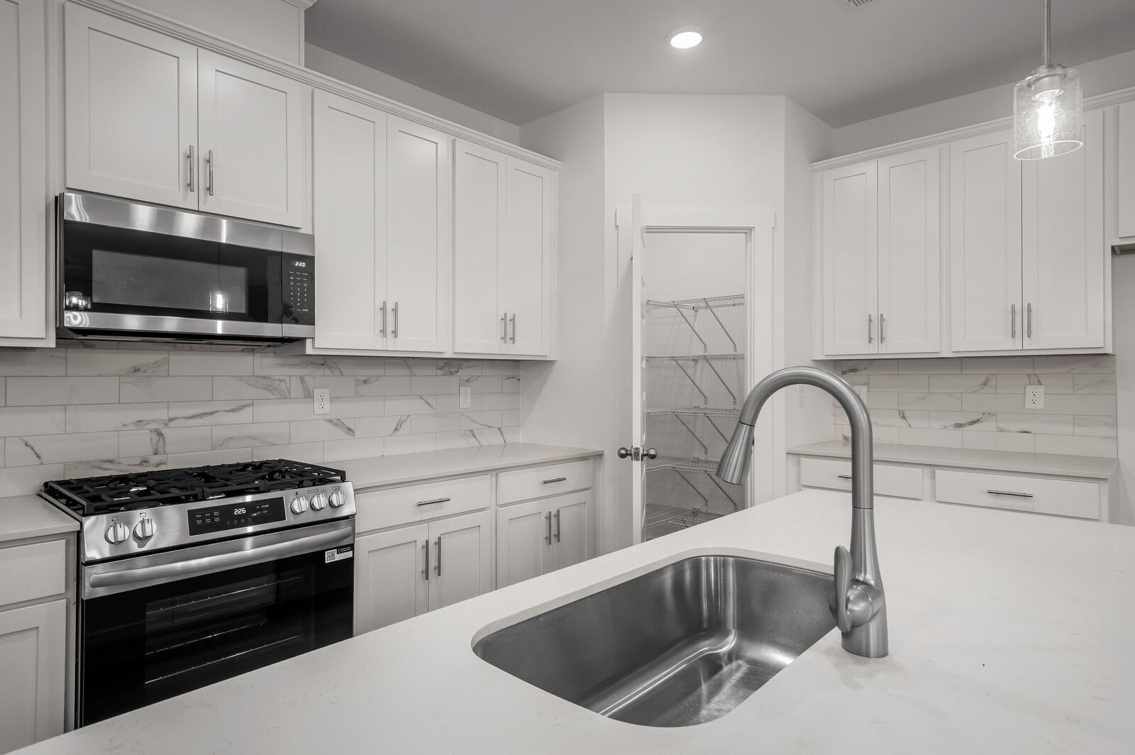 Modern kitchen with white cabinets, quartz countertops, and walk-in pantry in The Logan C floor plan, White House, TN.