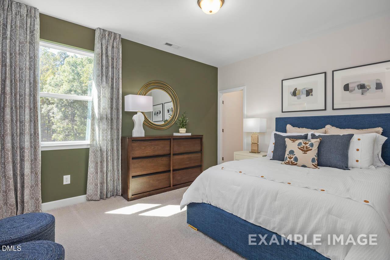 Cozy secondary bedroom with green accent wall, blue upholstered bed, dresser, and window view in The Hickory II C, Wake Forest, NC