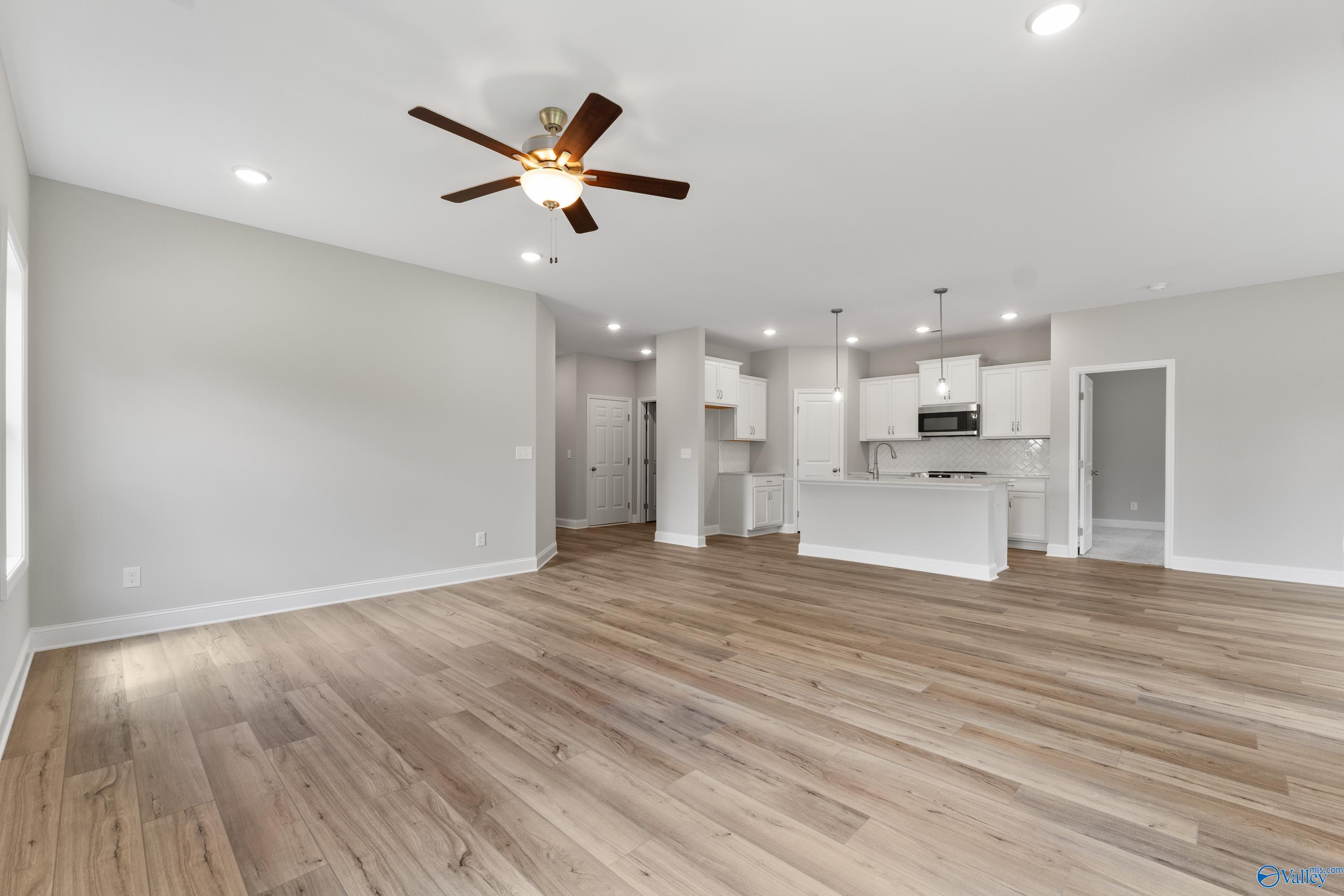 Open-concept living and kitchen with white cabinets, large island, ceiling fan, and hardwood floors in Davidson Homes The Franklin, Huntsville, AL