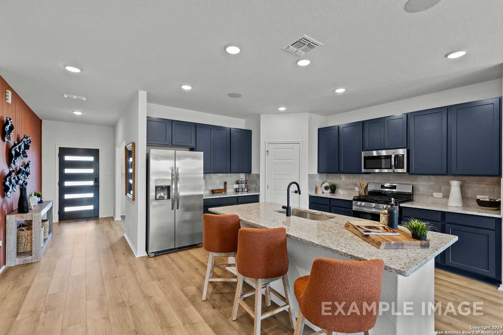 Modern navy blue kitchen with granite island, stainless appliances, orange stools in Davidson Homes Douglas G, Bricewood, San Antonio