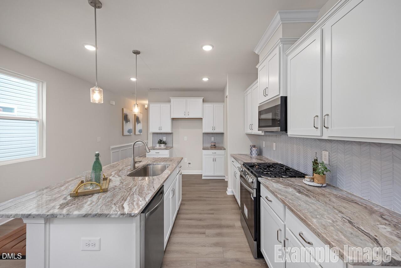 Modern kitchen with white shaker cabinets, veined granite island, stainless gas range in The Carter C home, Lillington, NC