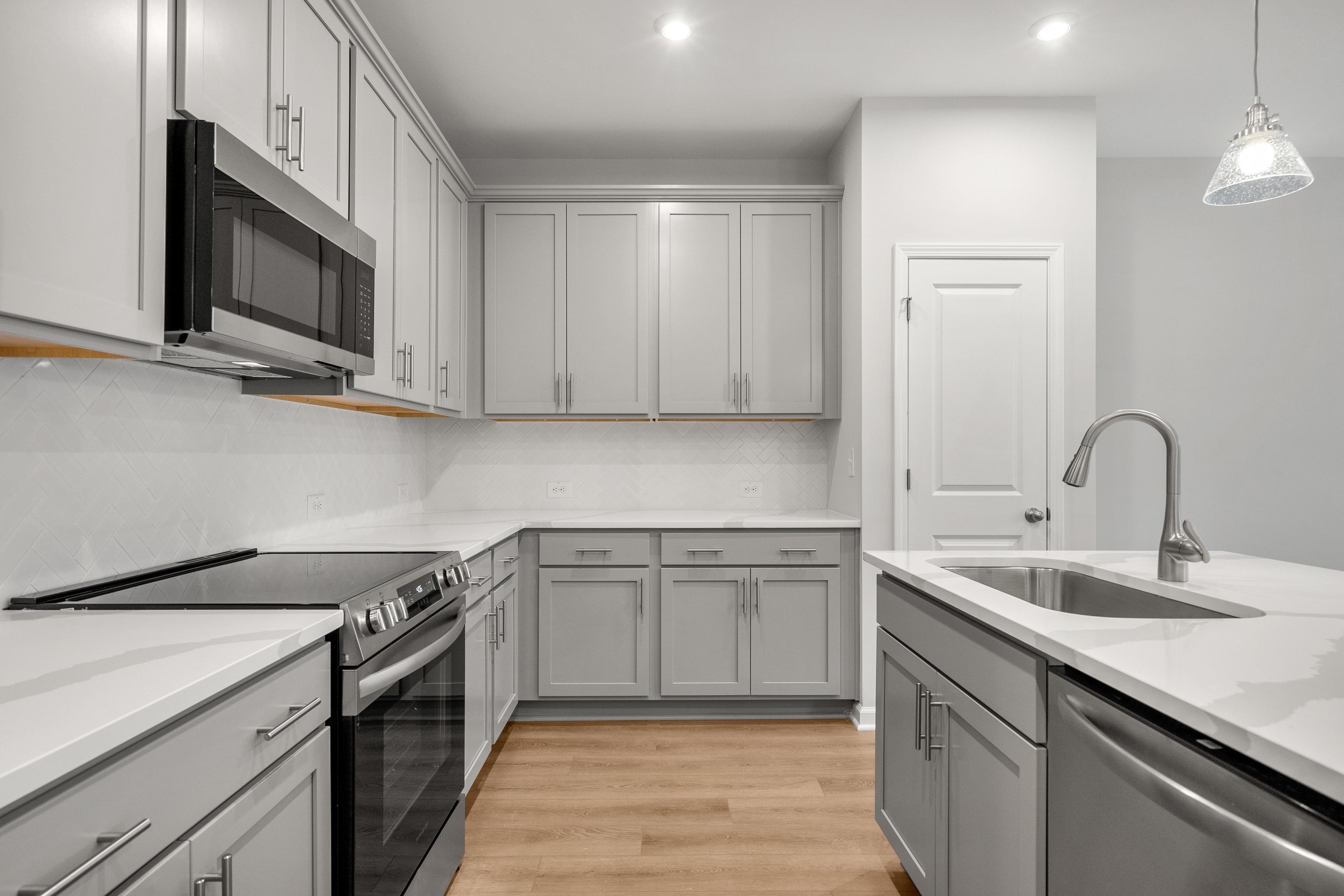Modern kitchen in The Durant A featuring shaker cabinets, quartz island sink, stainless appliances, subway tile backsplash