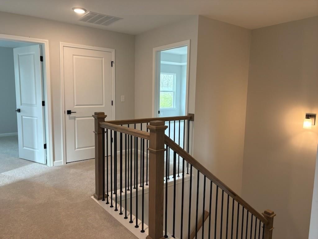Upstairs hallway featuring wooden staircase with black balusters and bedroom doors in The Hickory B 5-bedroom home, Winder, Georgia