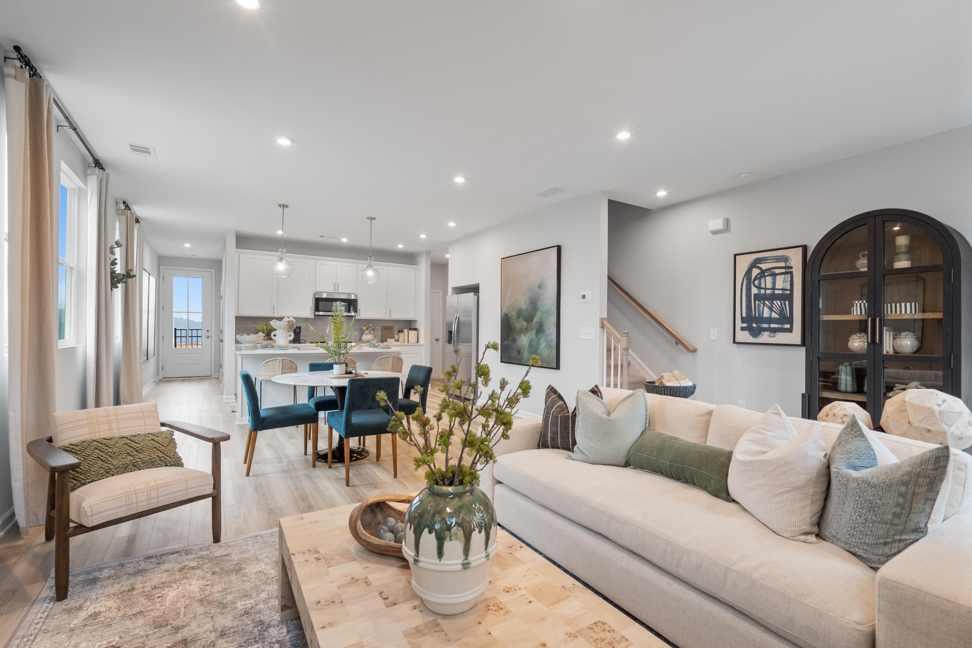 Open-concept living room at Retreat at North Main in Lillington NC with gray sectional sofa, hardwood floors, arched mirror, and modern kitchen