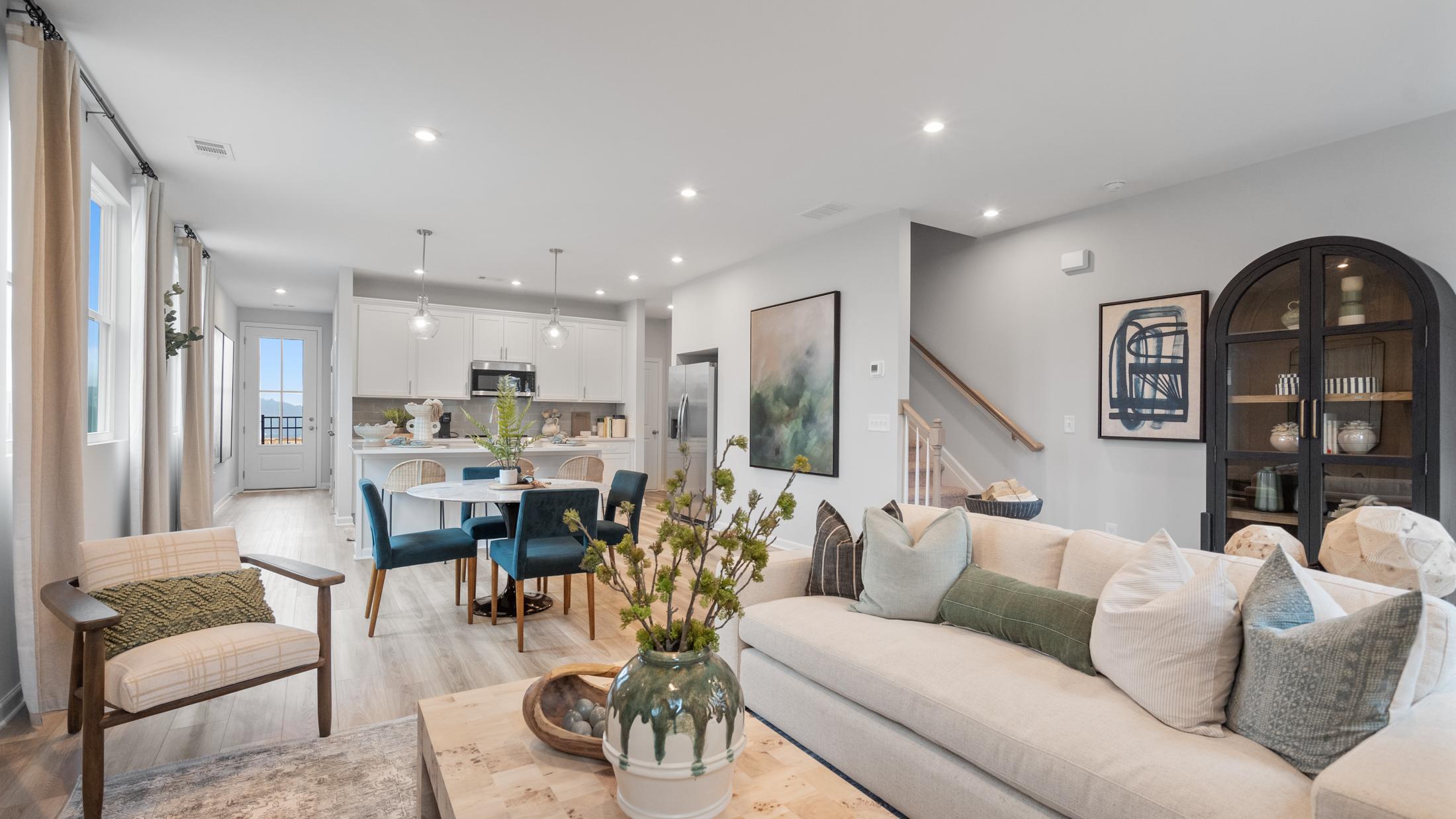 Open-concept living room at Retreat at North Main in Lillington NC with gray sectional sofa, hardwood floors, arched mirror, and modern kitchen