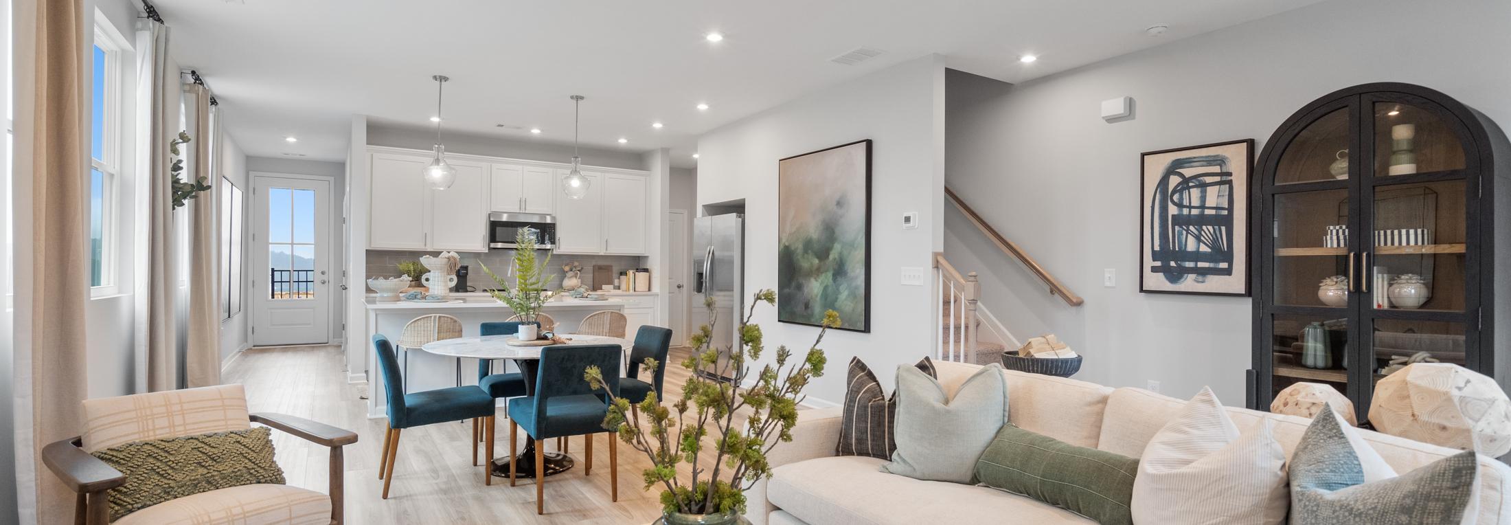 Open-concept living room at Retreat at North Main in Lillington NC with gray sectional sofa, hardwood floors, arched mirror, and modern kitchen