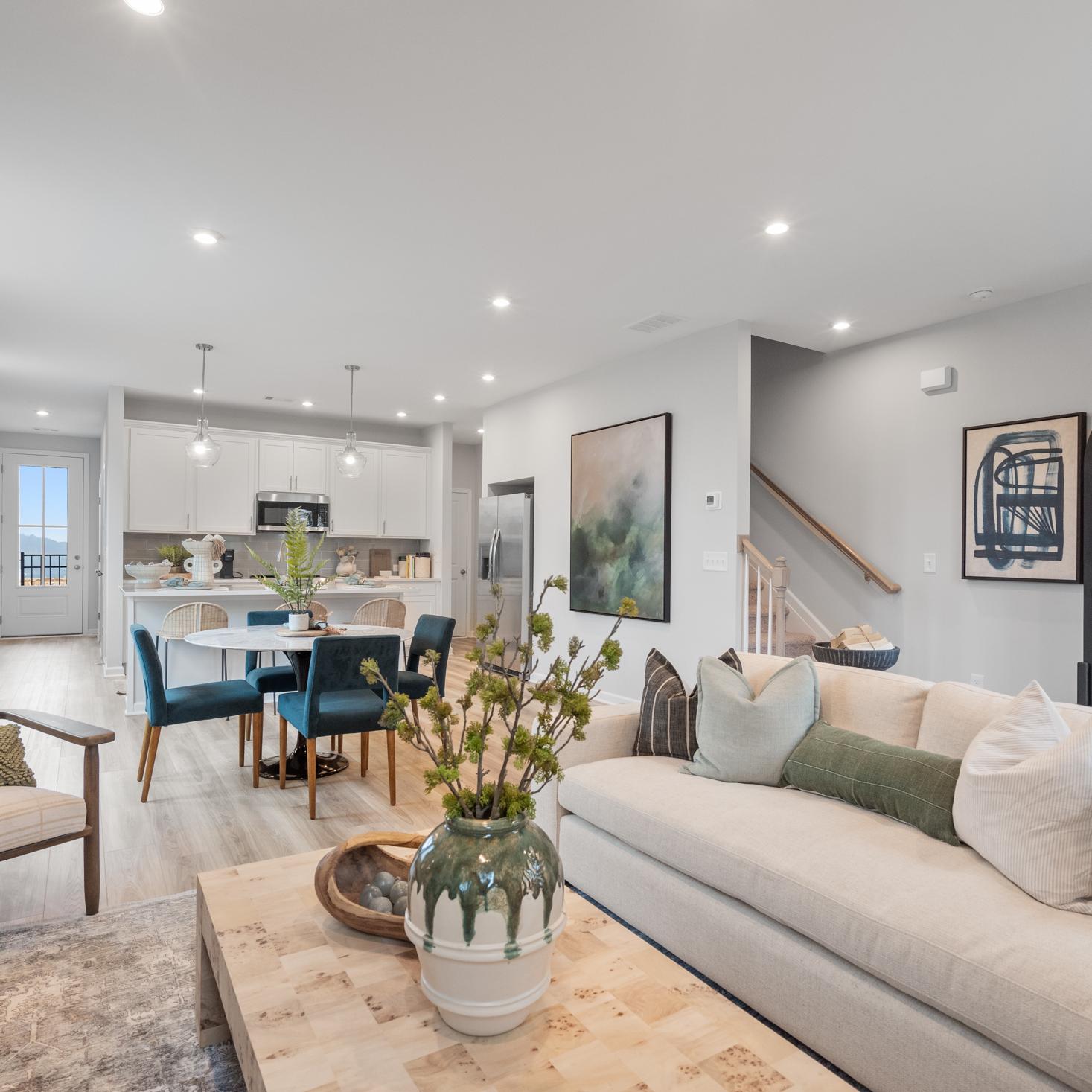 Open-concept living room at Retreat at North Main in Lillington NC with gray sectional sofa, hardwood floors, arched mirror, and modern kitchen