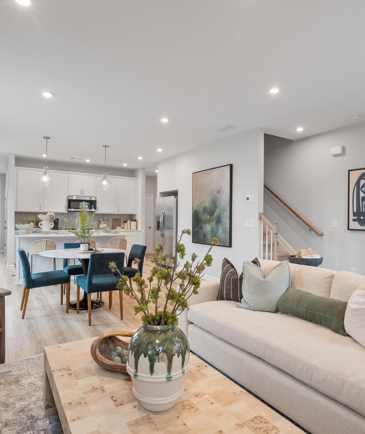 Open-concept living room at Retreat at North Main in Lillington NC with gray sectional sofa, hardwood floors, arched mirror, and modern kitchen