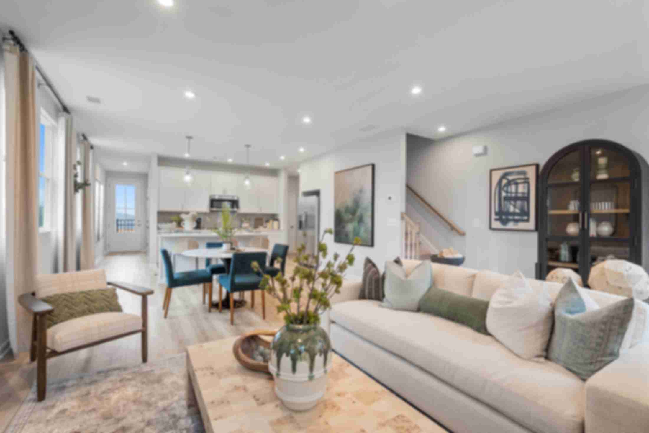 Open-concept living room at Retreat at North Main in Lillington NC with gray sectional sofa, hardwood floors, arched mirror, and modern kitchen