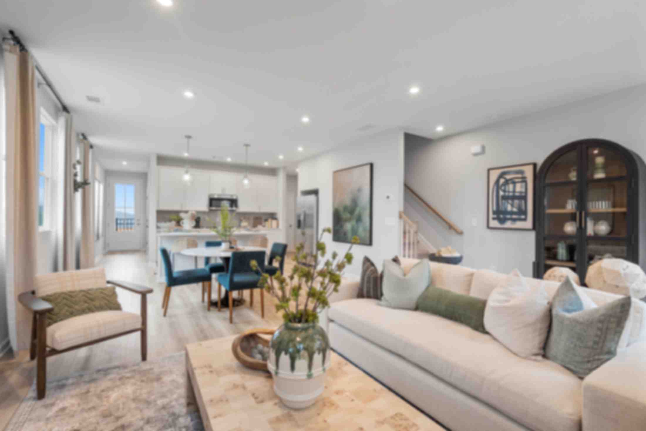 Open-concept living room at Retreat at North Main in Lillington NC with gray sectional sofa, hardwood floors, arched mirror, and modern kitchen