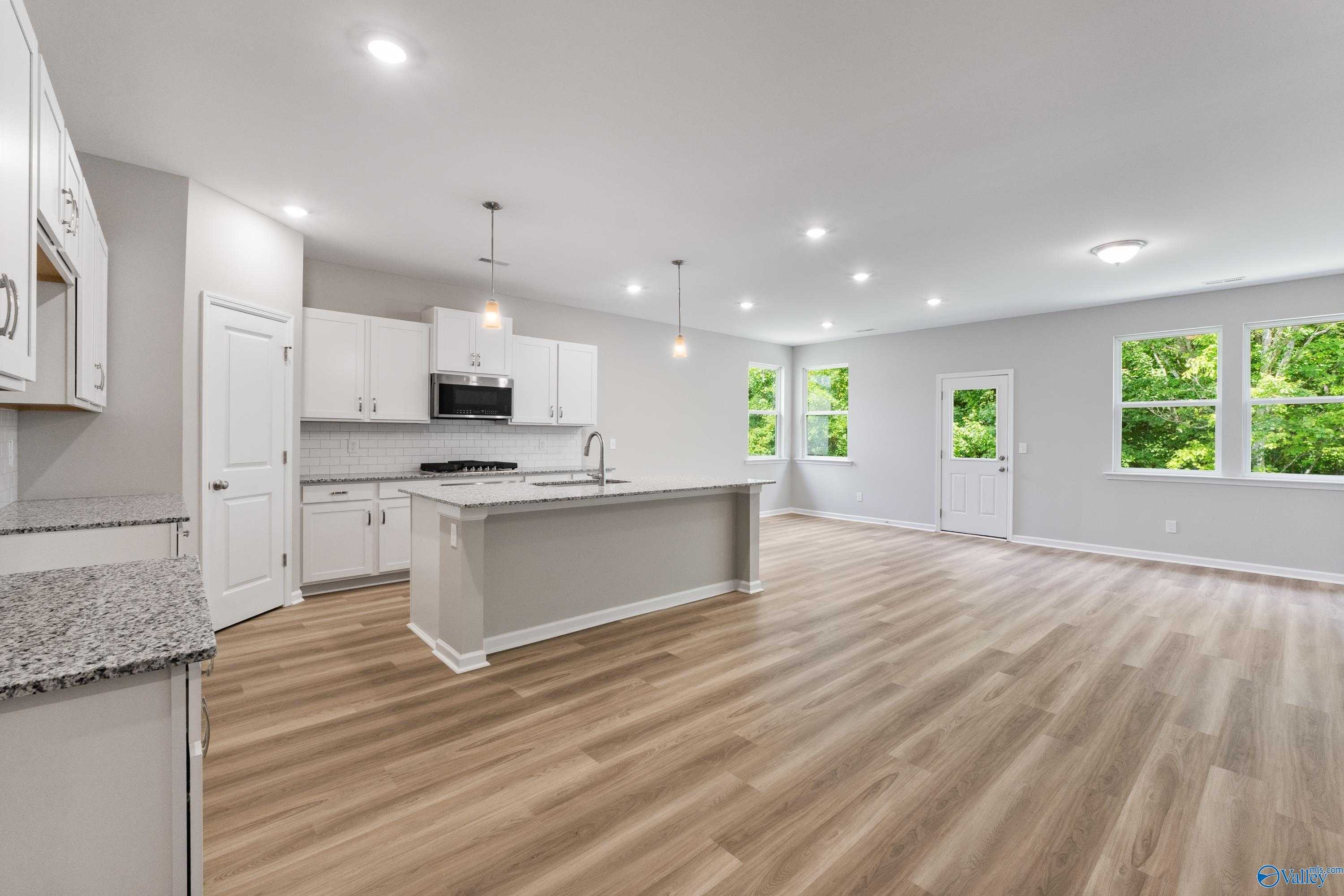 Open-concept kitchen with granite island, white cabinets, stainless appliances, and hardwood floors in Davidson Homes The Phoenix, Hazel Green, AL