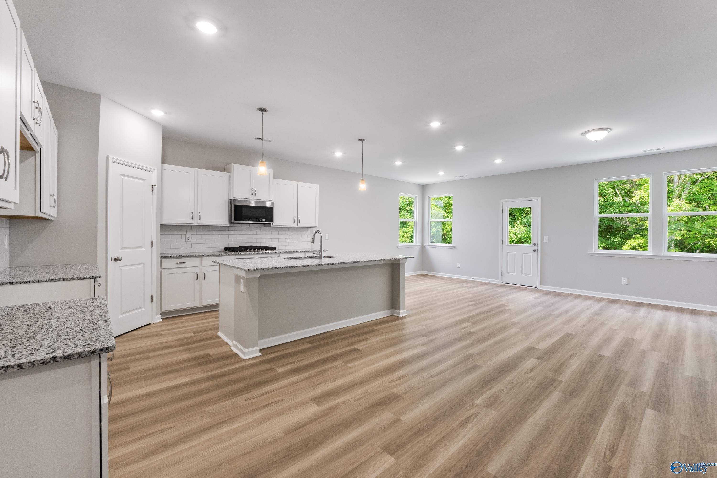 Open-concept kitchen with white cabinets, granite island, stainless appliances, and hardwood floors in The Phoenix, Hazel Green, AL