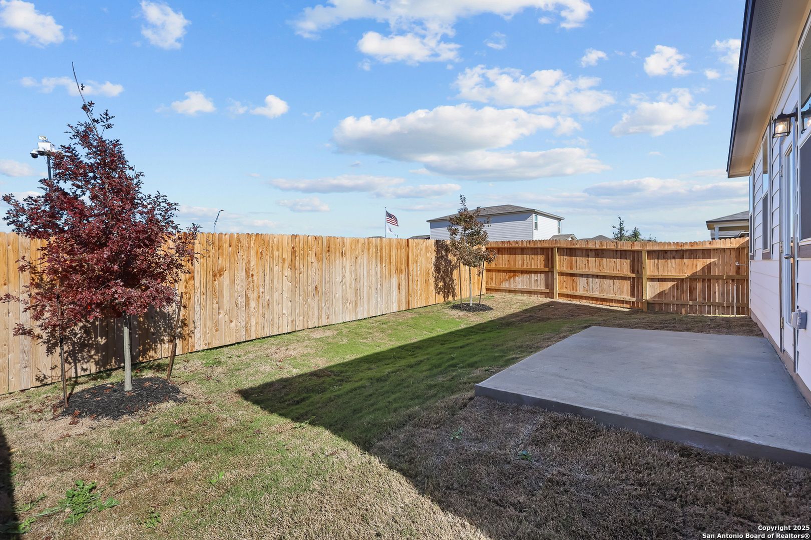 Fenced backyard with red maple tree, fresh sod lawn, concrete patio, and American flag in Davidson Homes The Colorado B, Applewhite Meadows, San Antonio