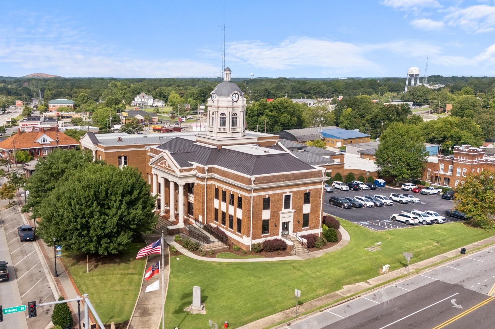 Aerial view of historic red brick courthouse in Winder Georgia with clock tower, American flag, and tree-lined streets