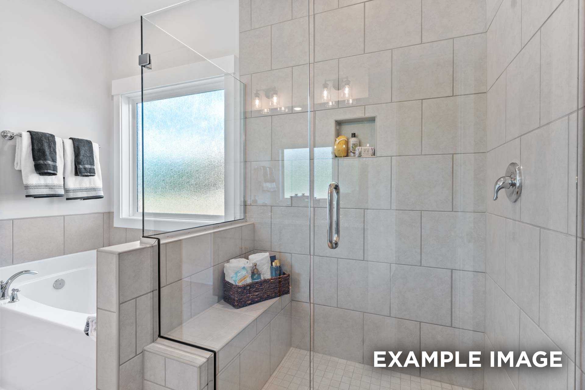 Spacious master bathroom in The Franklin C with frameless glass shower, soaking tub, and tiled bench