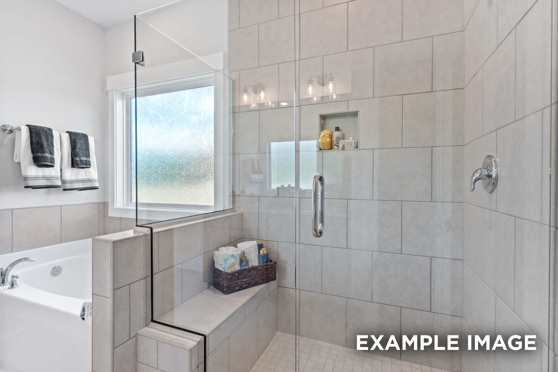 Spacious master bathroom in The Franklin C with frameless glass shower, soaking tub, and tiled bench