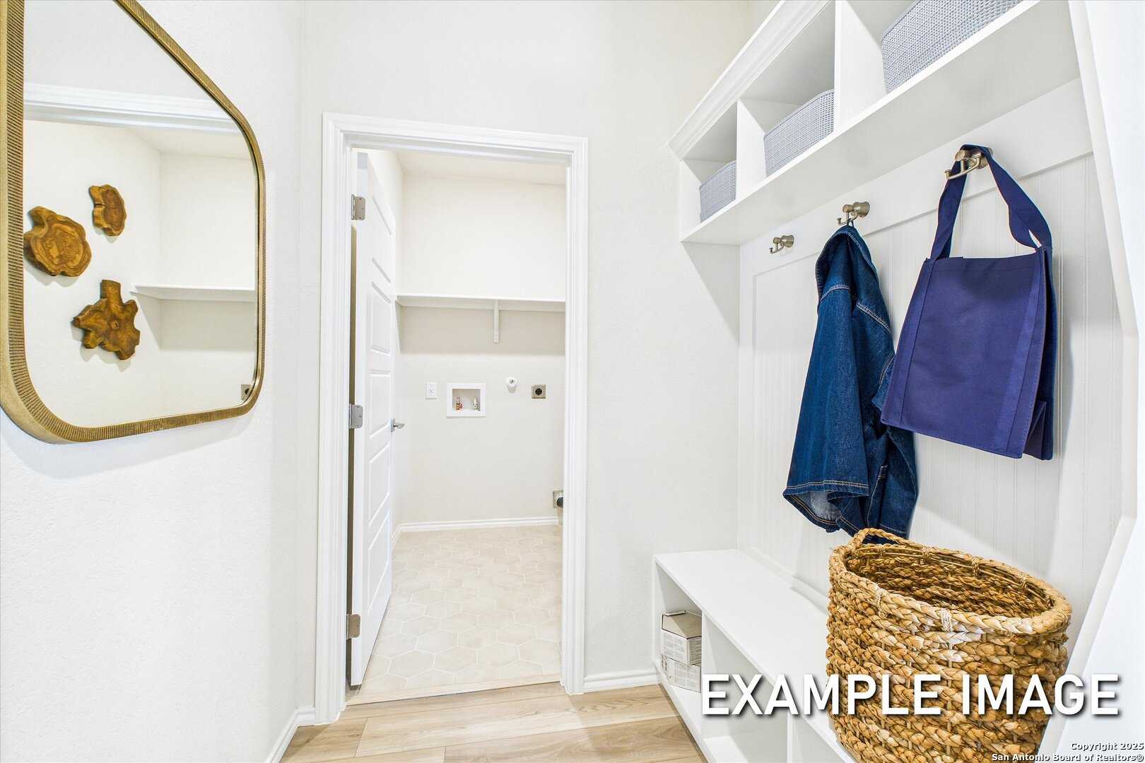 Modern mudroom with white built-in cabinets, coat hooks, blue jacket, purple bag, gold mirror, in Davidson Homes The Brazos C, Agave San Antonio Texas