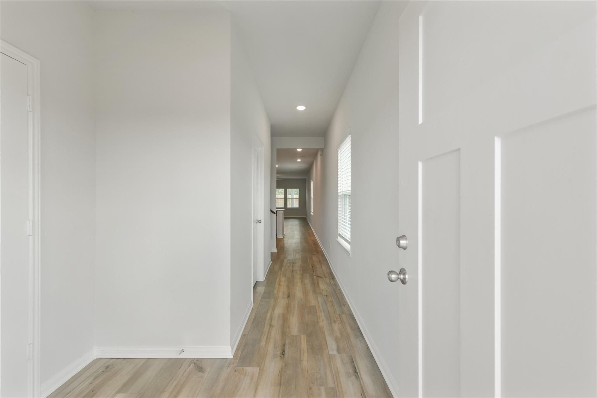 Long hallway with light wood floors, white walls, and recessed lighting in The Sabine F 4-bedroom home, Dayton, Texas