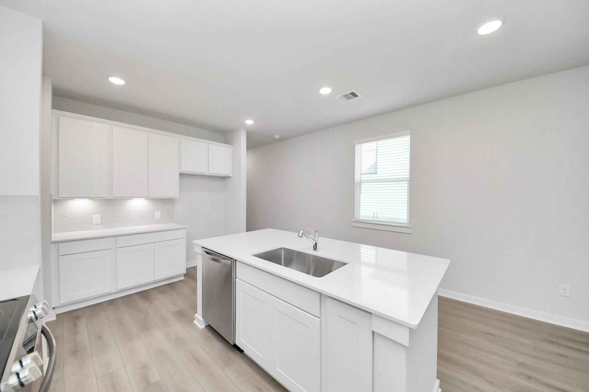 Modern kitchen with white cabinets, quartz island, and stainless steel appliances in The Frio F plan, Liberty Estates.