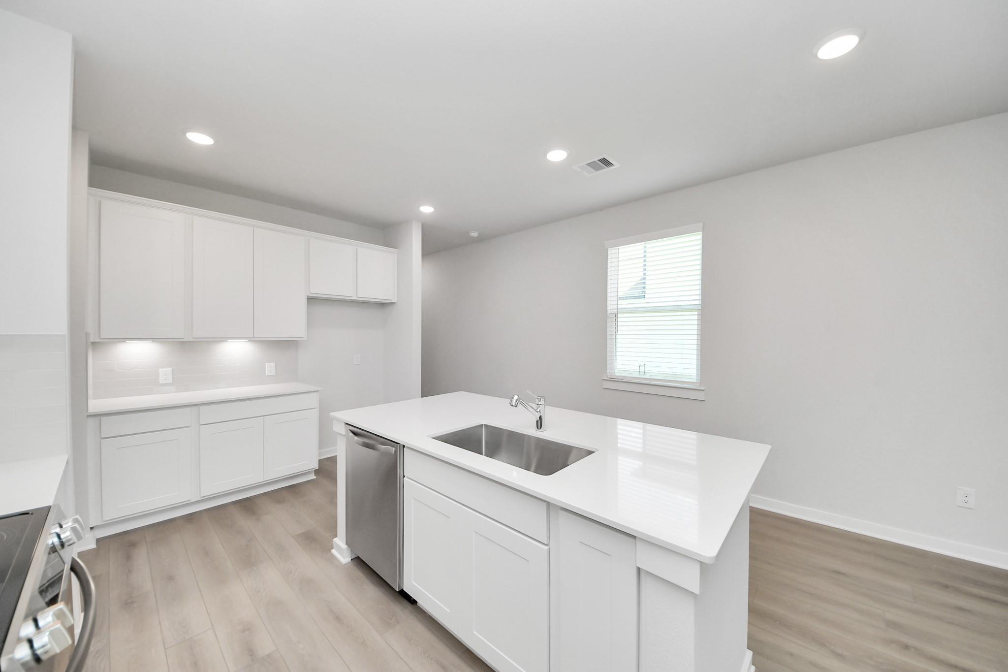 Modern kitchen with white cabinets, quartz island, and stainless steel appliances in The Frio F plan, Liberty Estates.