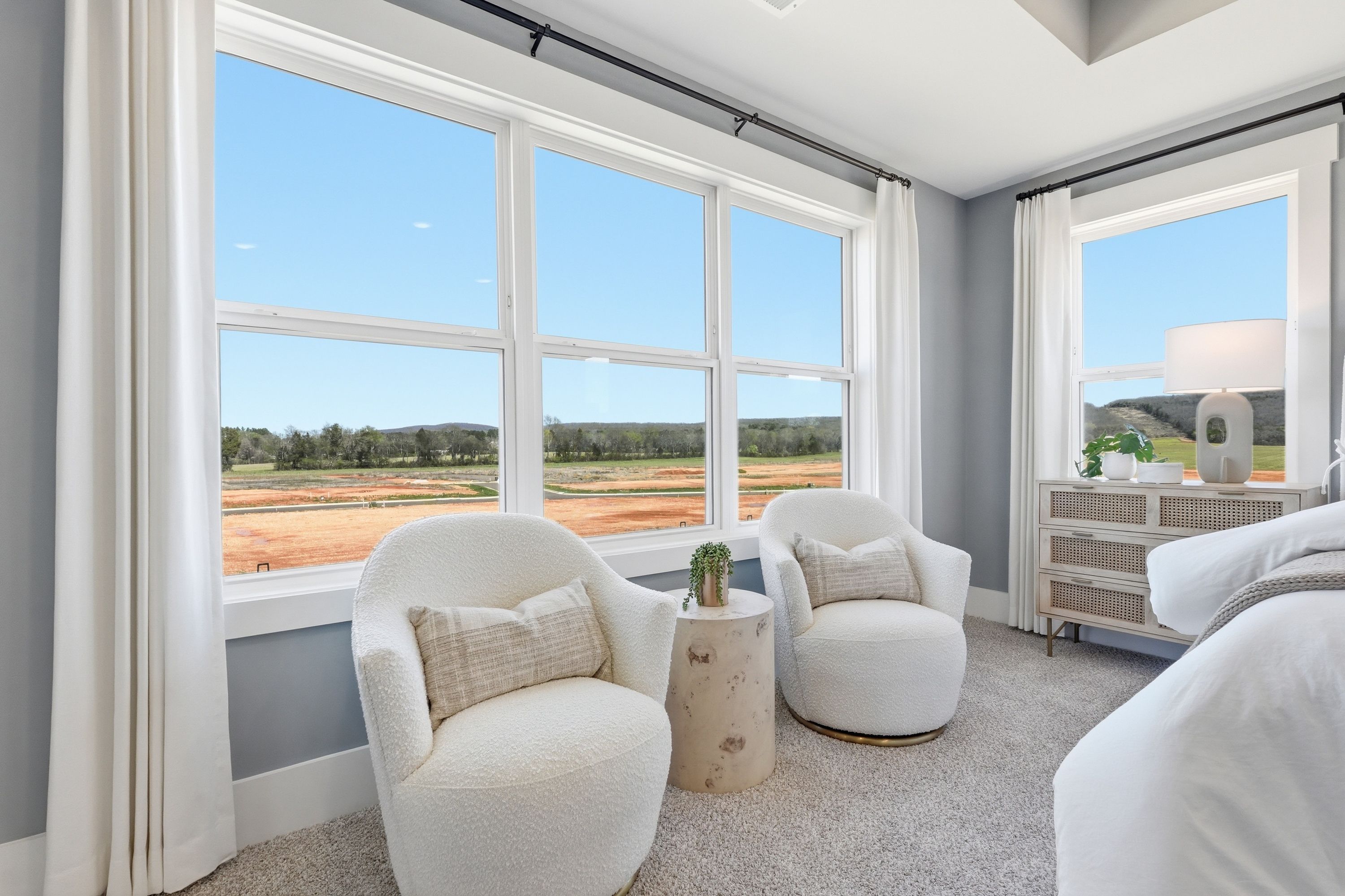 Cozy bedroom nook at Berry Cove in New Market Alabama with plush white armchairs large windows overlooking fields and neutral gray walls