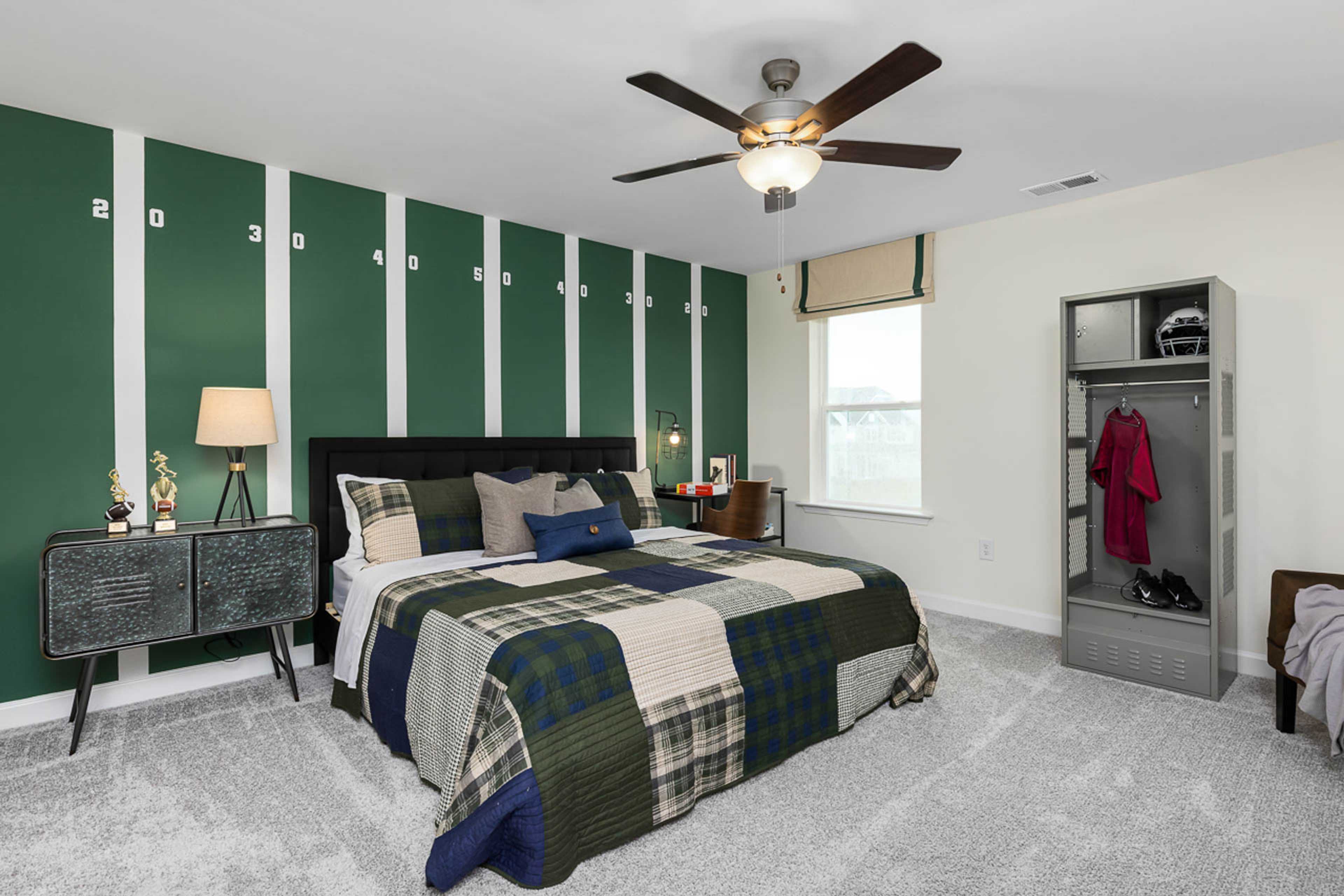 Football-themed bedroom at Weatherford East in Angier NC with green striped walls, plaid bedding, ceiling fan, and sports locker