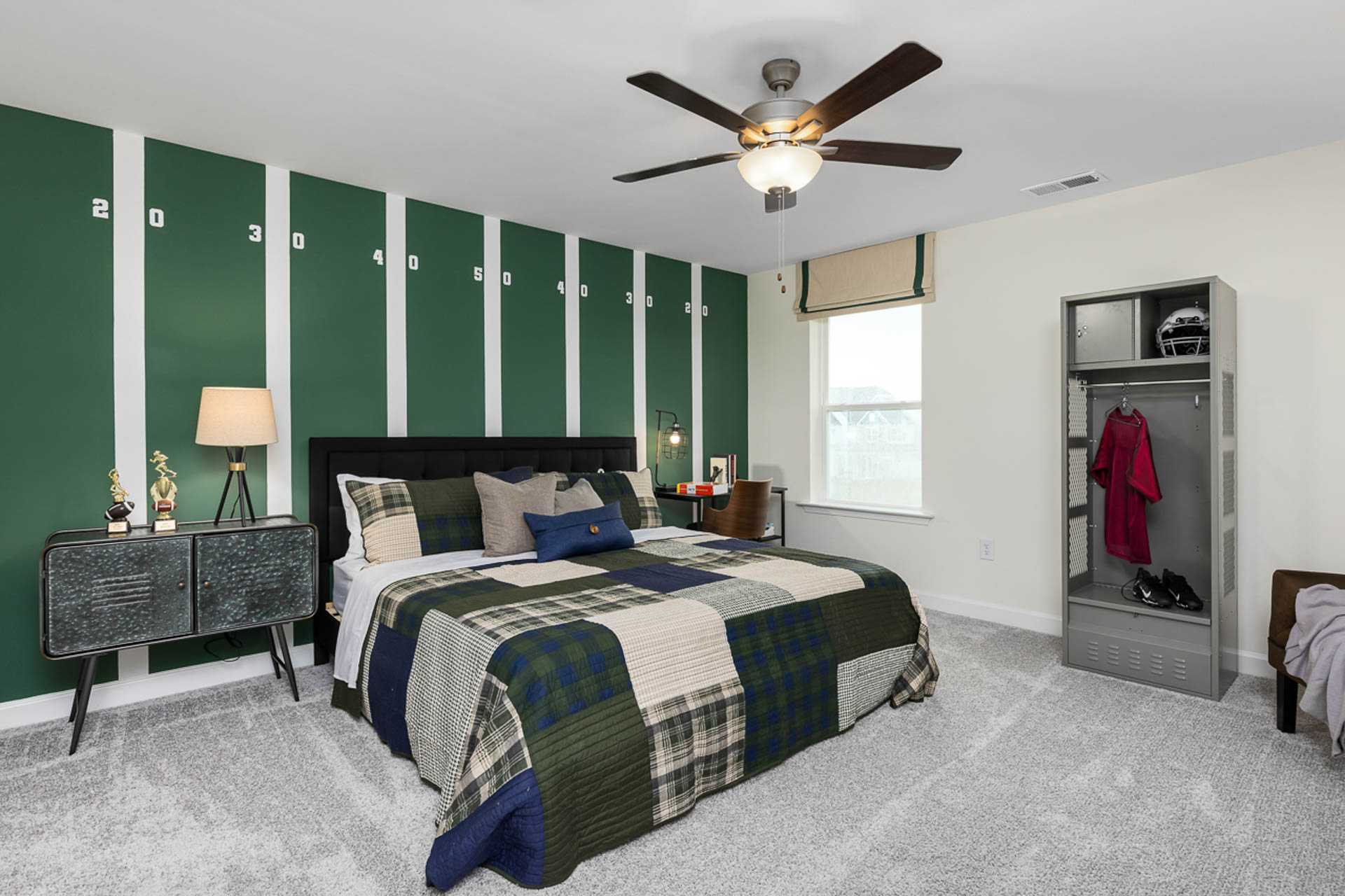 Football-themed bedroom at Weatherford East in Angier NC with green striped walls, plaid bedding, ceiling fan, and sports locker