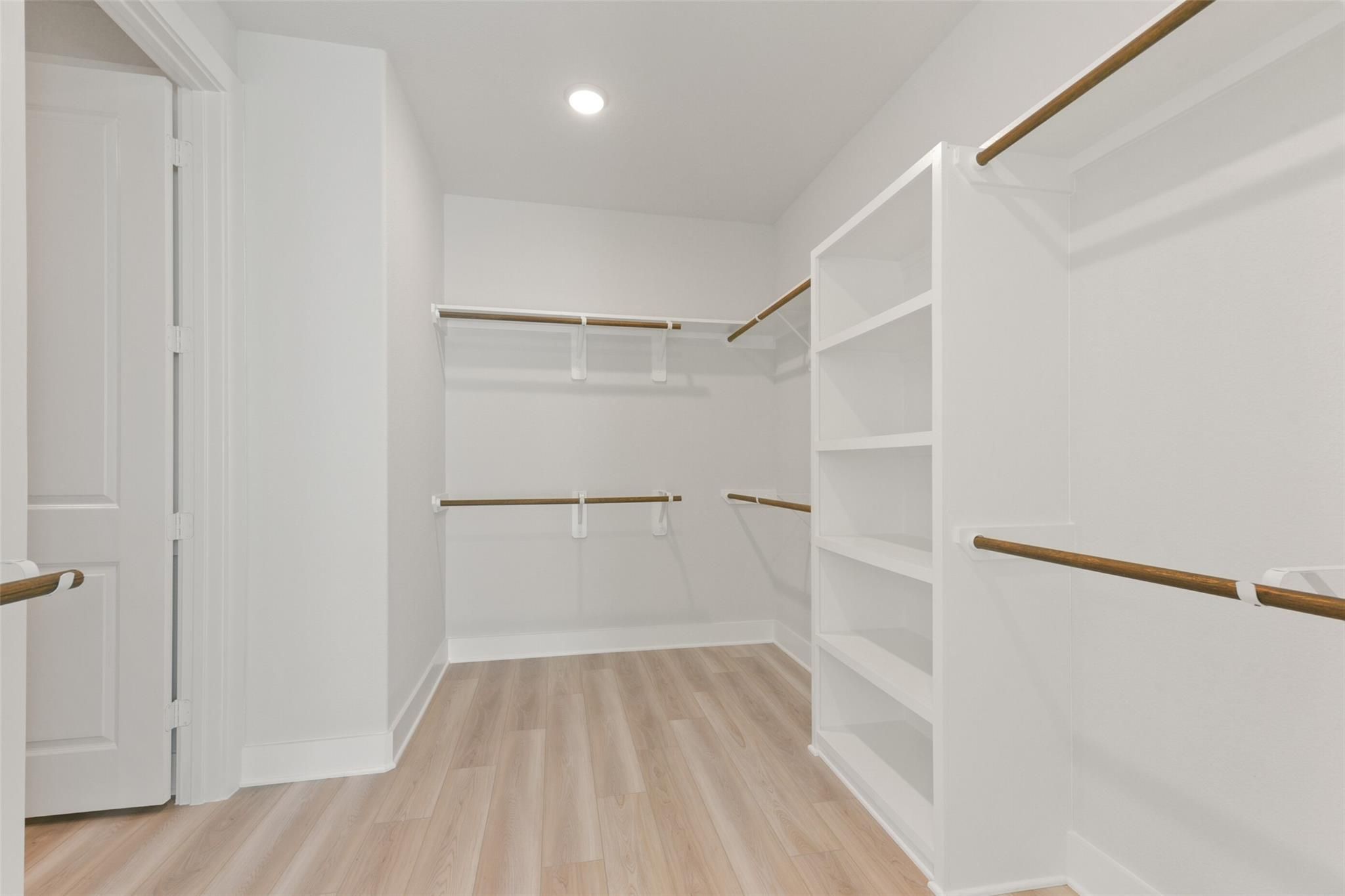 Spacious walk-in closet with built-in wood shelves and hanging rods on white walls in Davidson Homes The Edward C, Lago Mar, Texas City