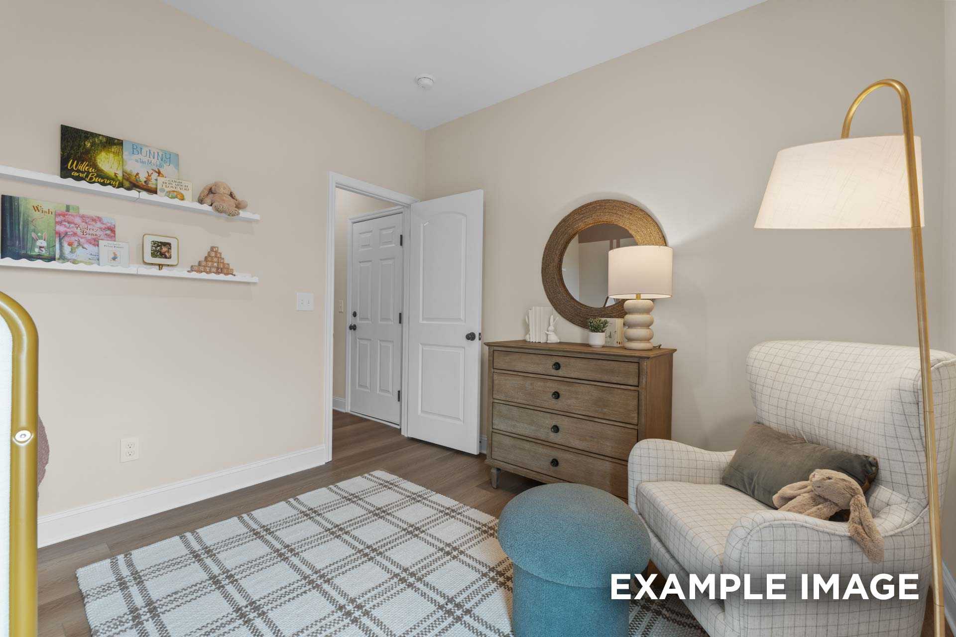 Cozy nursery in The Laurel home design by Davidson Homes featuring beige walls, wooden dresser, bookshelf with toys, plush armchair, and checkered rug