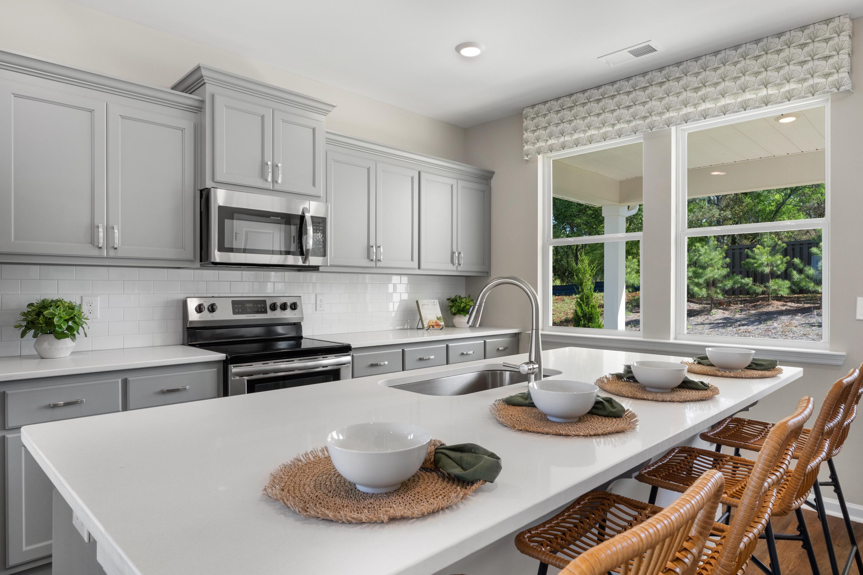 Spacious modern kitchen in Evergreen Mill, Madison AL with gray shaker cabinets, white island, stainless appliances, and window views