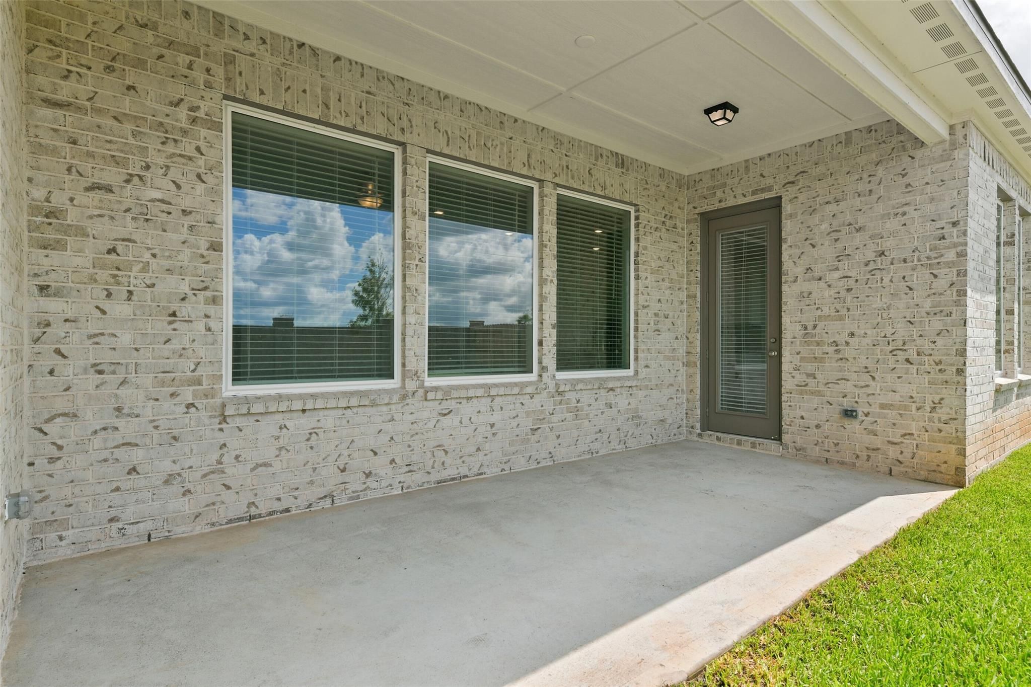 Beige brick exterior of 1-story 3-bedroom home with large windowed patio, sliding door, and ceiling fan in Davidson Homes The Edward A, Lago Mar, Texas City