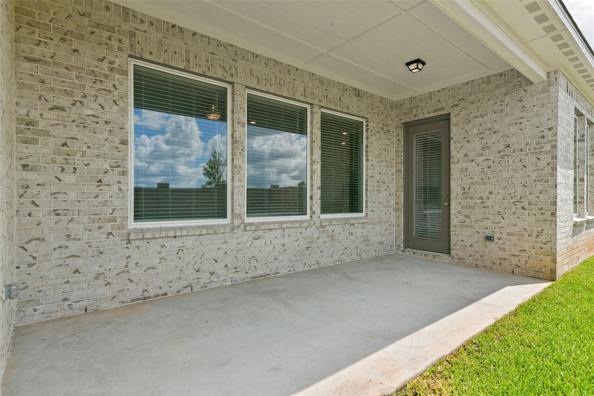 Beige brick exterior of 1-story 3-bedroom home with large windowed patio, sliding door, and ceiling fan in Davidson Homes The Edward A, Lago Mar, Texas City