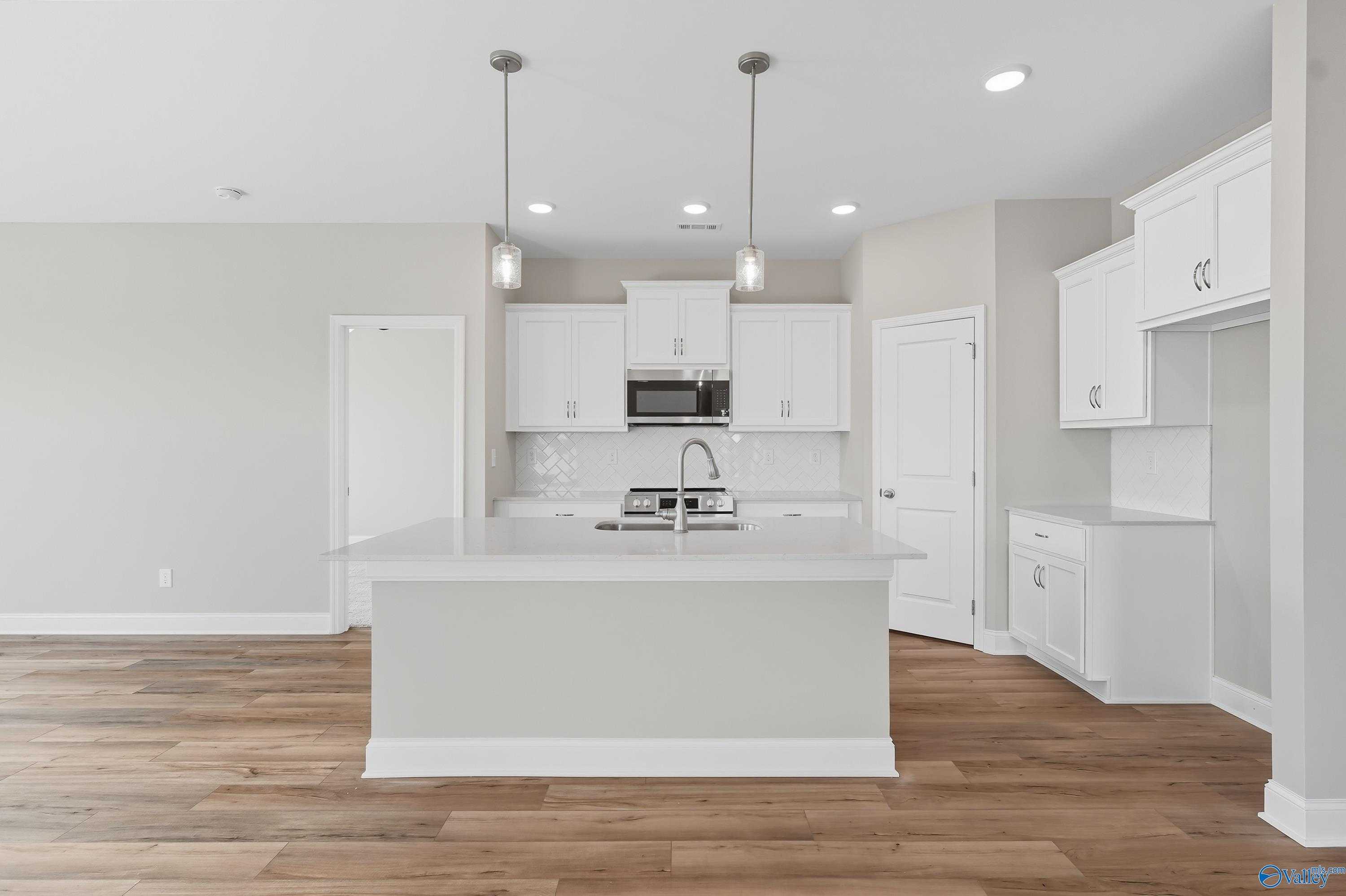 Modern white shaker kitchen with center island sink, stainless appliances, pendant lights, and hardwood floors in Davidson Homes The Franklin, Meridianville, AL