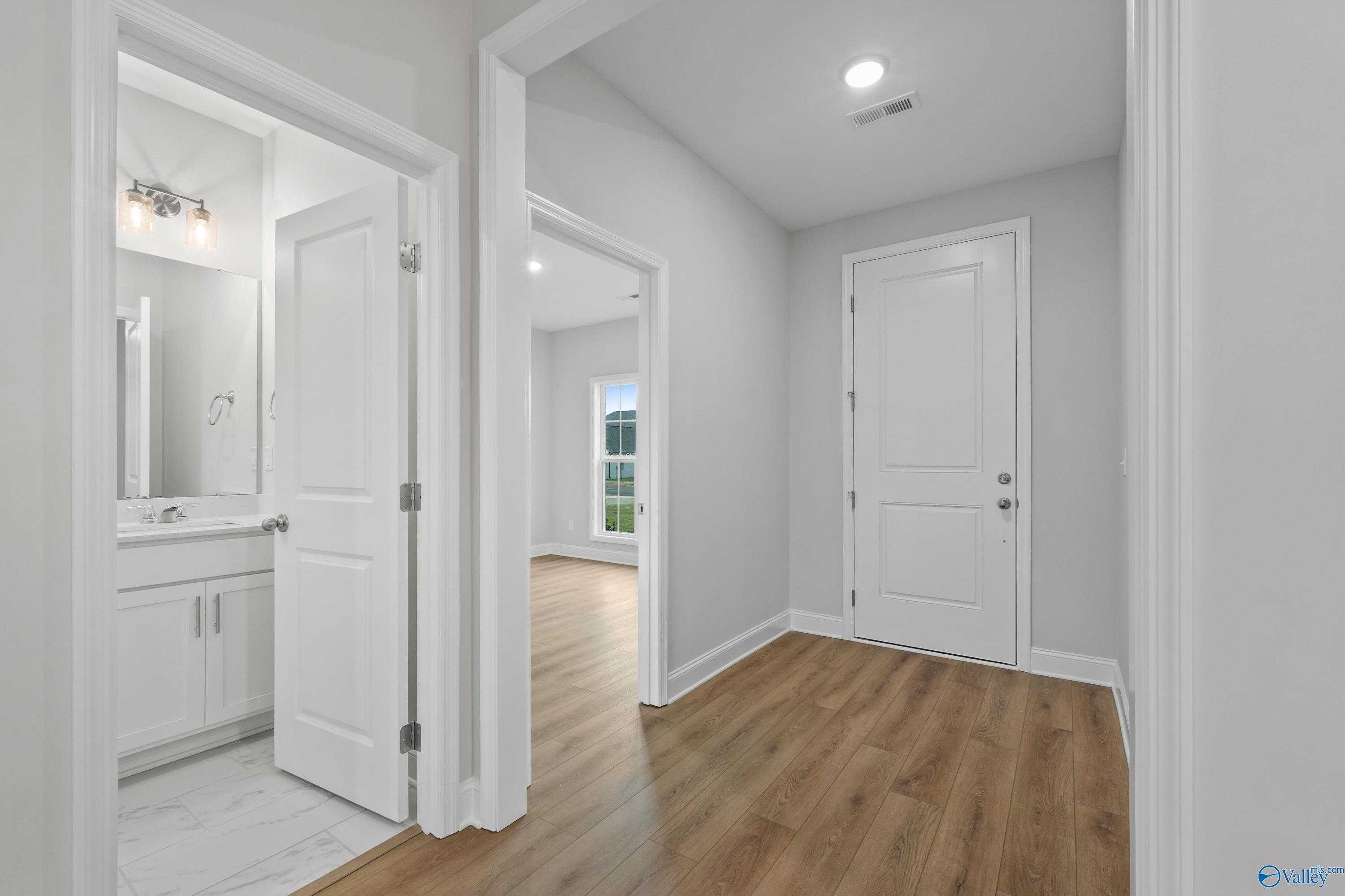 Bright hallway with guest bathroom vanity, mirror, and open doors to bedrooms in Davidson Homes The Lanier, Harvest, Alabama